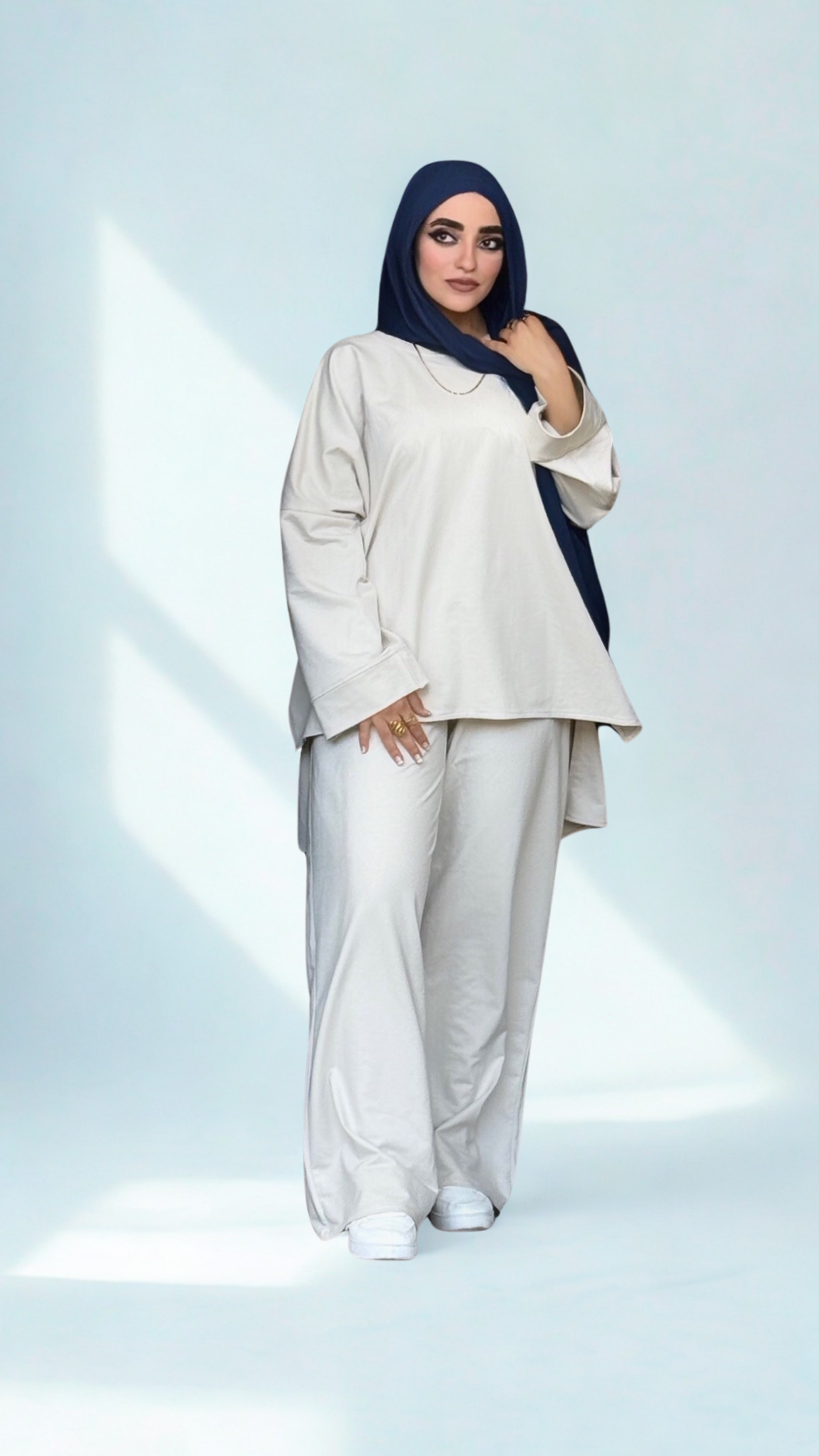 Woman wearing a white outfit with a blue hijab on a light gray background