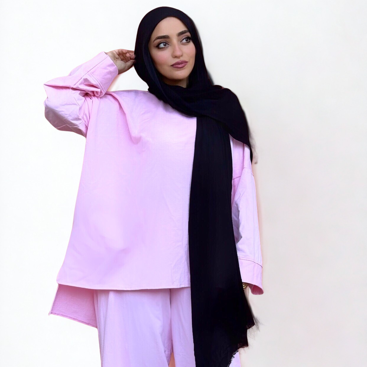 Woman wearing a light pink outfit with a black hijab on a white background