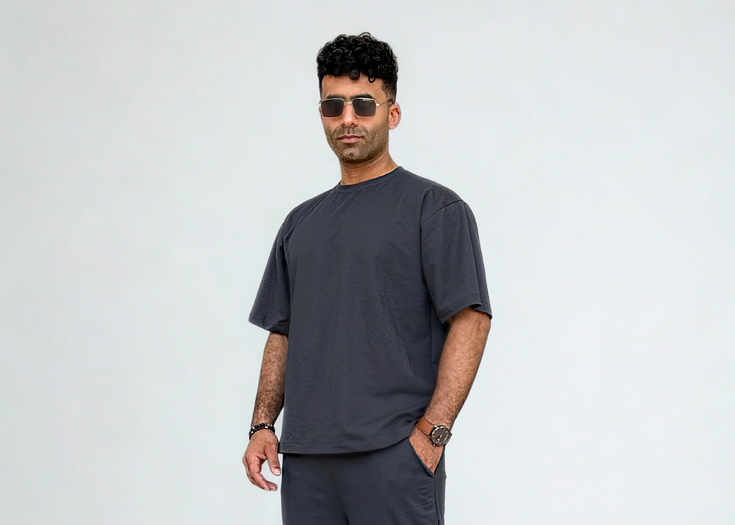 Man wearing a dark gray t-shirt and pants with white sneakers on a white background