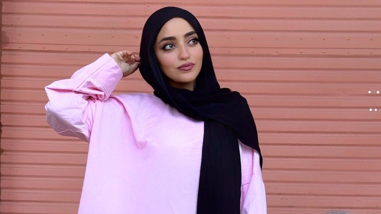 Model wearing a pink outfit with a black hijab against a pink background