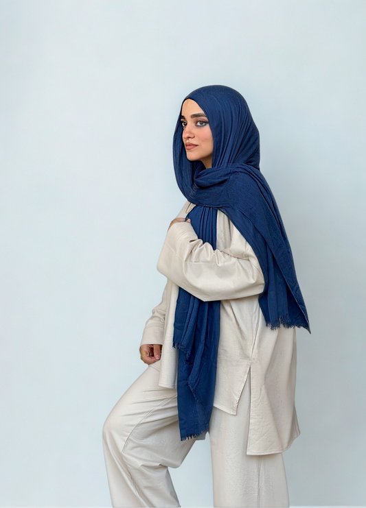 Person wearing a navy hijab and beige outfit against a light background
