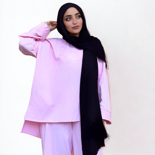 Woman wearing a light pink outfit with a black hijab on a white background